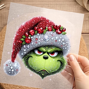 Könnte beinhalten: Ein Diamond-Painting-Aufkleber mit einem grünen Charakter mit finsterem Blick und roten Augen, der eine rot-weiße Weihnachtsmütze trägt, die mit roten Edelsteinen, grünen Blättern und funkelnden, weißen Kristallen in strukturierter Optik verziert ist.