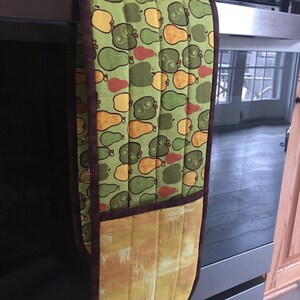 May include: A green and brown oven mitt with a pear and apple pattern. The mitt has a pocket on the back side.