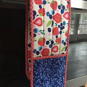 May include: A red and blue oven mitt with a strawberry and blueberry pattern. The mitt has a pocket on the back for holding hot items.