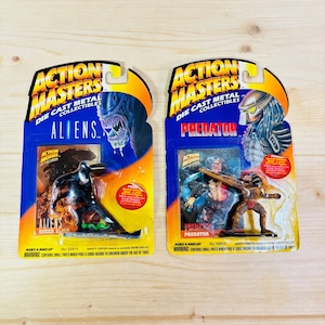 Puede incluir: Dos figuras coleccionables de metal fundido a presión Action Masters, una con "Aliens" y otra "Predator". Cada figura está en su embalaje original, con vibrantes acentos azules y amarillos. El embalaje incluye ilustraciones de personajes y el texto "Action Masters."