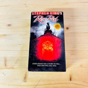 May include: A Stephen King's Rose Red VHS tape. The cover features a red-lit house with a dark, ominous sky. The text reads "EVERY HOUSE HAS A STORY TO TELL... THIS ONE WILL KILL YOU."