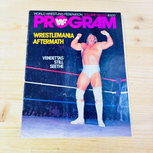 Puede incluir: Un programa de lucha libre vintage con un luchador en calzoncillos y botas blancas, levantando los brazos. La portada presenta el texto "PROGRAM" en rosa, con "WRESTLEMANIA AFTERMATH" y "VENDETTAS STILL SEETHE" en amarillo y blanco.