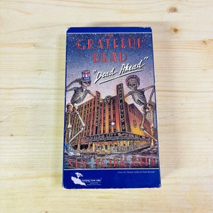 May include: A vintage VHS tape for "The Grateful Dead: Dead Ahead" featuring a colorful illustration. The cover art depicts skeletons, the Radio City Music Hall, and the text "New York City."