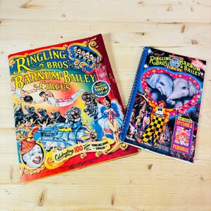 May include: Two vintage Ringling Bros. and Barnum & Bailey Circus books. The larger book is red, yellow, and blue with a picture of a clown, tigers, and elephants. The smaller book is blue, red, and yellow with a picture of a clown and two elephants. Both books have the text "Ringling Bros. and Barnum & Bailey Circus" on the cover.
