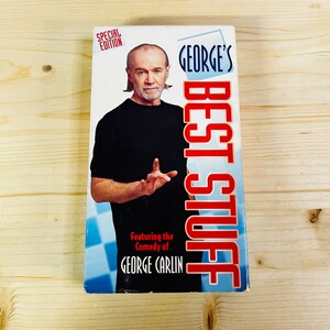 Puede incluir: Un libro titulado "George's Best Stuff" con George Carlin en la portada. La portada tiene un patrón de cuadros azules y blancos en la parte inferior y texto rojo y blanco. Las palabras "Special Edition" están en la parte superior.