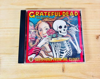 May include: A CD case featuring the album "Skeletons from the Closet" by The Grateful Dead. The cover art includes a woman holding a rose, a skeleton playing a cymbal, and the text "Grateful Dead" and "The Best Of".