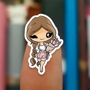 May include: A sticker featuring a cartoon girl with brown hair, wearing a white shirt and pink shorts, holding a bouquet of pink flowers.