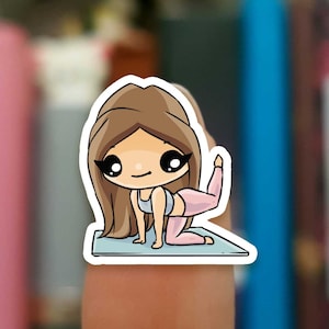 Op de afbeelding: Een cartoon sticker van een vrouw die een yogapose aanneemt op een blauwe mat. Ze heeft lang bruin haar, een roze top en roze leggings.