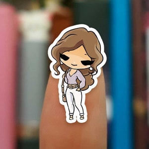 May include: A sticker featuring a cartoon illustration of a woman with brown hair, wearing a light purple top, white pants, and a brown belt. She is holding a brown purse and has a small brown bag on her shoulder.