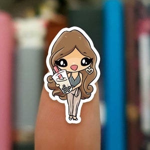 May include: A sticker of a cartoon woman with brown hair, wearing a white top and pants, holding a cup of boba tea. She has a heart-shaped earring and is smiling.