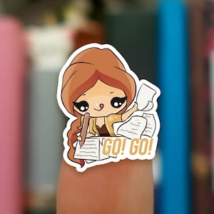 May include: A sticker featuring a cartoon girl with brown hair and a yellow shirt, surrounded by papers and a pencil. The sticker says "GO! GO!" in yellow letters.