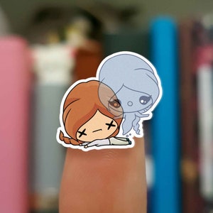 May include: A sticker featuring a cartoon illustration of a girl with brown hair and a ghost with a blue body. The girl is lying down with her eyes closed and the ghost is hovering above her.