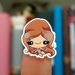 Puede incluir: Una pegatina de una niña de dibujos animados con el pelo largo y rojo que lleva un bañador rosa y está rodeada de burbujas.