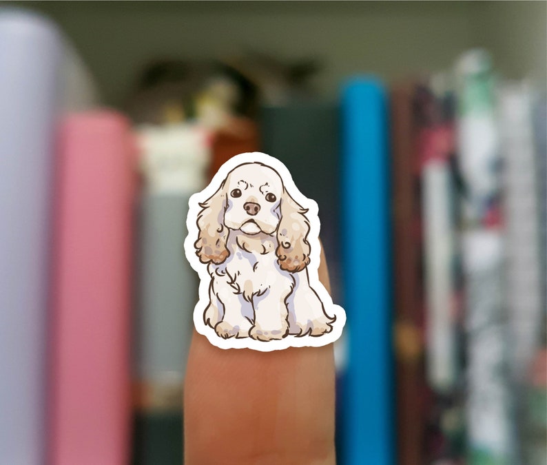 May include: A sticker featuring a cartoon illustration of a white and brown cocker spaniel dog with floppy ears. The dog is looking directly at the viewer.
