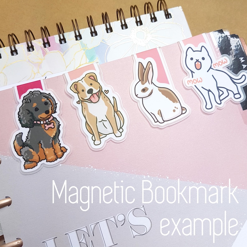 May include: A set of four magnetic bookmarks featuring cartoon illustrations of a dog, a cat, a rabbit, and a puppy. The bookmarks are printed on clear plastic and have a pink background. The text "Magnetic Bookmark" and "LET'S example" is printed on the bottom of the bookmarks.