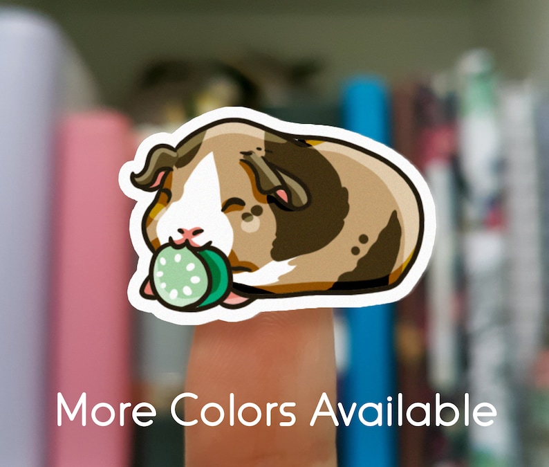 May include: A sticker featuring a cartoon guinea pig with brown, white, and tan fur, holding a green cucumber slice. The text "More Colors Available" is displayed in white at the bottom of the image.