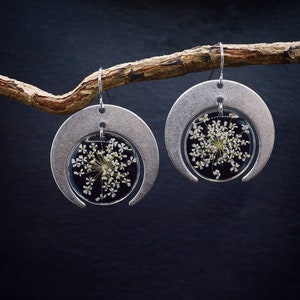 May include: A pair of silver crescent moon earrings with a small white flower pressed inside each earring.