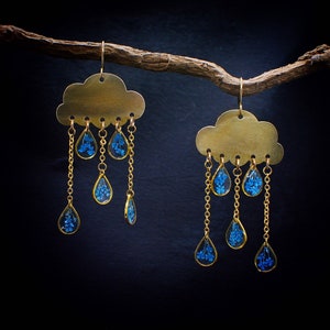 May include: A pair of gold-tone earrings shaped like clouds with dangling blue raindrop charms filled with tiny blue flowers.