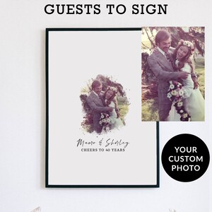May include: A white framed print with a black and white photo of a couple in a watercolor effect. The text "Mauro & Shirley CHEERS TO 40 YEARS" is below the photo. The print is on a white wall above a couch with white pillows.