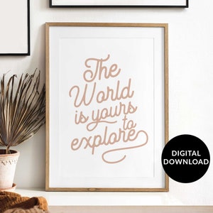 May include: A printable digital download of a motivational quote in a light brown color. The quote reads "The World is yours to explore". The quote is framed in a light wood frame and is displayed on a white wall.