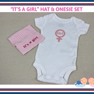 May include: A white onesie with the text "Girl" and a pink female symbol. A pink and white striped hat with the text "It's a girl" is also included.