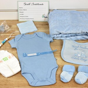 May include: A baby gift set with a blue blanket, a blue onesie, a blue bib, a blue and white striped hat, a diaper, a pair of blue and white striped socks, a blue pacifier, and a wooden bead teether.