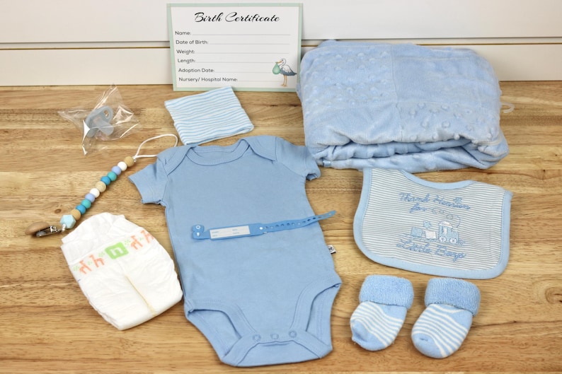 May include: A baby gift set with a blue blanket, a blue onesie, a blue bib, a blue and white striped hat, a diaper, a pair of blue and white striped socks, a blue pacifier, and a wooden bead teether.