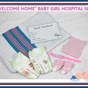May include: A baby girl hospital set with a white blanket with blue and red stripes, a pink hat, a pair of pink booties, a diaper, a pair of socks, a pink bracelet with a blank tag, and a birth certificate card.