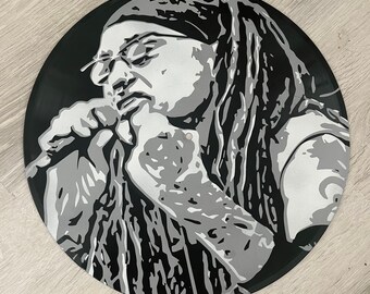 May include: Black and white stencil art of a person with long hair singing into a microphone. The person is wearing a bandana and a tank top.