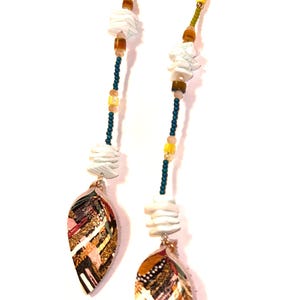 Puede incluir: Pendientes colgantes largos con un colgante en forma de hoja. Los pendientes presentan una combinaci&oacute;n de cuentas blancas, marrones, amarillas y verdes. Los colgantes de hoja tienen un dise&ntilde;o de patchwork colorido con detalles dorados.