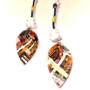 May include: A pair of dangle earrings with a leaf-shaped pendant. The pendants feature a colorful mosaic design with gold, red, and green accents. The earrings have a beaded chain with white, yellow, and teal beads, and white abstract shapes.