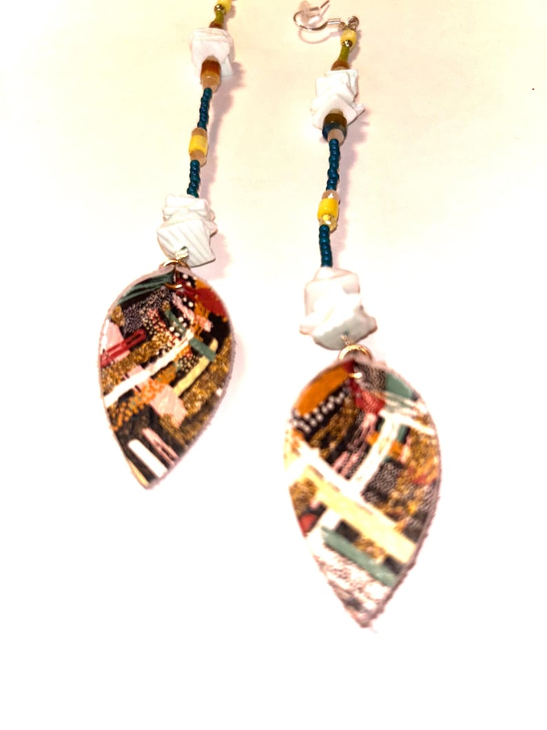 Puede incluir: Pendientes colgantes con colgantes en forma de hoja. Los colgantes presentan un dise&ntilde;o de mosaico colorido con detalles dorados, rojos y verdes. Los pendientes tienen una cadena de cuentas con cuentas blancas, amarillas y turquesas, y formas abstractas blancas.