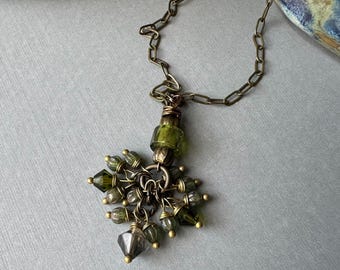 Colgante de cuentas de vidrio verde oliva con detalles de latón.