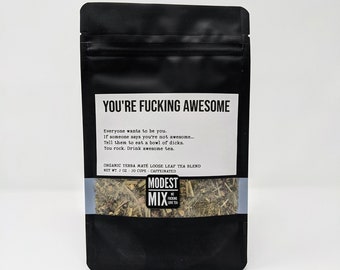 May include: A black pouch with a white label that reads "YOU'RE FUCKING AWESOME" and contains a loose leaf tea blend. The label also includes the text "ORGANIC YERBA MATE LOOSE LEAF TEA BLEND", "NET WT. 2 OZ - 20 CUPS", and "CAFFEINATED". The pouch also features a logo that reads "MODEST MIX WE FUCKING LOVE TEA".