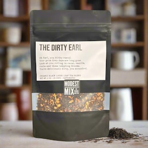 May include: A black bag of "The Dirty Earl" organic black loose leaf tea blend. The bag has a clear window showing the tea leaves and text that reads "Modest Mix We Fucking Love Tea". The net weight is 2 oz.