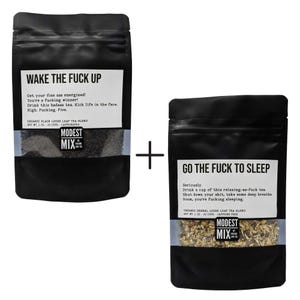 May include: Two black pouches of tea with white labels. One reads "WAKE THE FUCK UP" and the other "GO THE FUCK TO SLEEP". The tea blends are visible through the clear window. The brand name "MODEST MIX" is also visible.