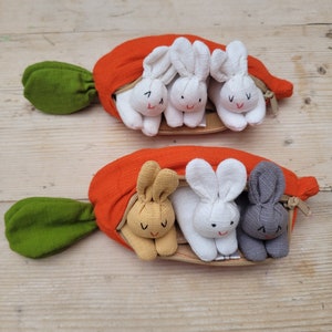 A carrot purse bursting with three bunnies 1 white 1 beige 1 grey