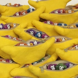 May include: A close-up of several yellow fabric pouches with zips. Each pouch is filled with small, colourful stuffed monkeys. The pouches are arranged in a pile, with some overlapping.