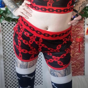 May include: A person wearing a black and red crop top and shorts set with a chain design. The crop top has the text "BITE RISK". The person is also wearing a black choker, wolf ears, and thigh-high socks.