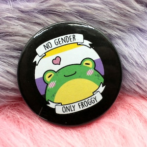 May include: A black button featuring a cartoon frog wearing a yellow, white and purple gender-neutral pride flag. The button reads "No Gender Only Froggy".