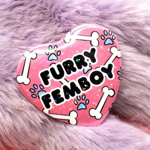 May include: Pink heart-shaped button with white bone and paw print designs. The button says "Furry Femboy" in black letters.