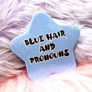 May include: A light blue star-shaped badge with the words "BLUE HAIR AND PRONOUNS" in black. The badge has a holographic glitter effect and is set against a fluffy, multi-coloured background.