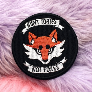 May include: Black embroidered patch with a red fox and the text "Hunt Tories Not Foxes" in white.