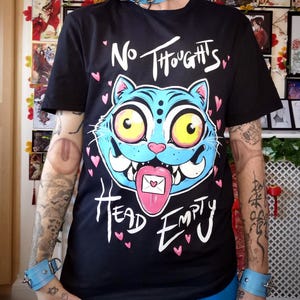 May include: Black t-shirt with a cartoon cat graphic that says "No Thoughts Head Empty". The cat is blue with yellow eyes and a pink tongue. The shirt is worn with blue accessories and a blue wig.