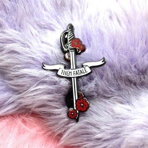 May include: A silver-toned enamel pin featuring a sword with red flowers and the text "Them Fatale".