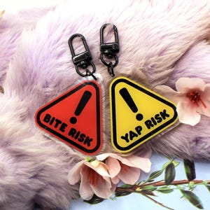 This 5cm triangluar acrylic charm is the perfect addition to any keyring or ita bag! The design features a triangluar red warning sign with the text '! BITE RISK' in large letters. It is double sided with a lobster clasp for easy fastening.