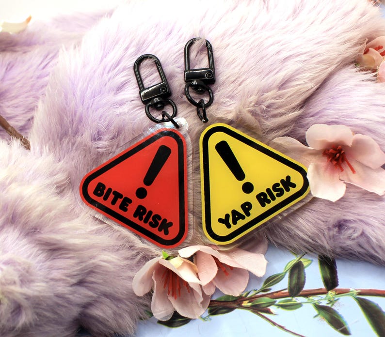 This 5cm triangluar acrylic charm is the perfect addition to any keyring or ita bag! The design features a triangluar red warning sign with the text '! BITE RISK' in large letters. It is double sided with a lobster clasp for easy fastening.