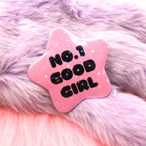 Peut inclure: Épinglette en forme d'étoile rose avec des paillettes et le texte "No. 1 Good Girl" en noir.