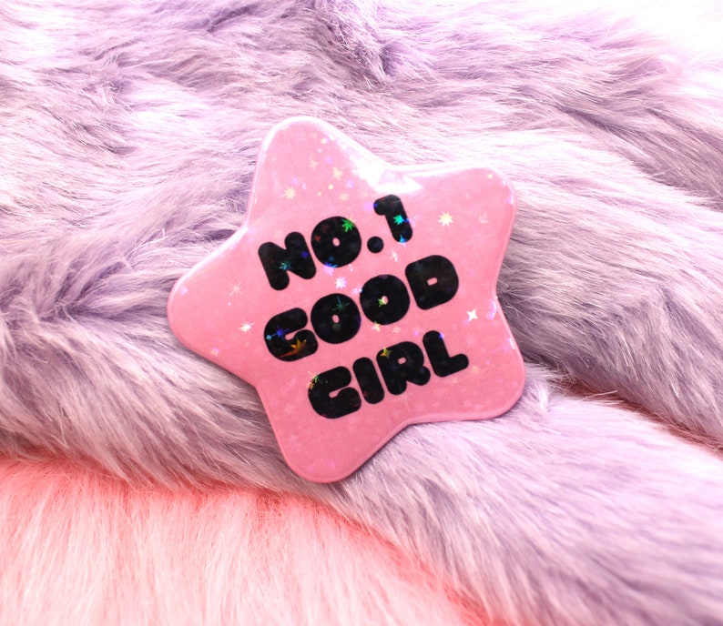 Puede incluir: Pin de estrella rosa con purpurina y el texto "No. 1 Good Girl" en negro.