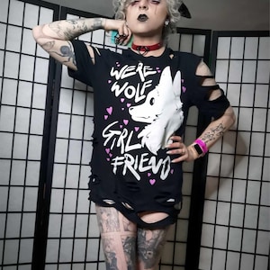 May include: A black t-shirt with a distressed look featuring a white wolf graphic and the text "Werewolf Girlfriend" with pink hearts.